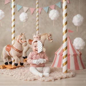 May include: A baby wearing a crown and pink outfit sits in front of a carousel scene. The scene includes toy horses, a circus tent, and cotton candy decorations. The background is a neutral color with hanging pennants.