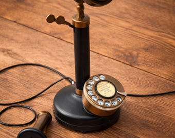 May include: Antique black and brass candlestick telephone with a rotary dial. The phone features a brass earpiece and mouthpiece, a black base, and a black cord. The phone is a vintage item.