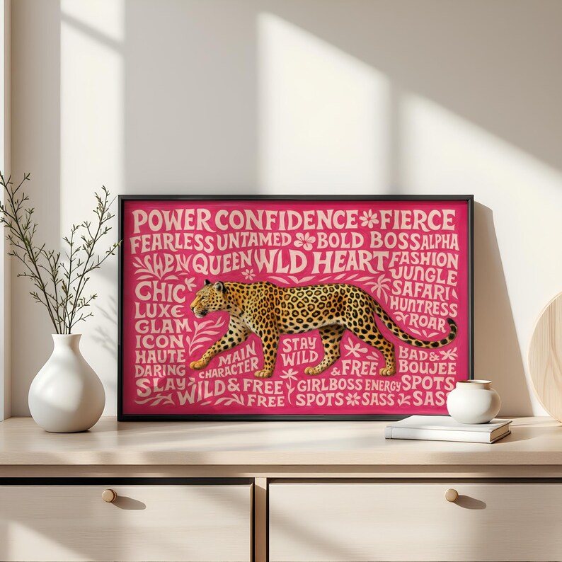 May include: A framed print featuring a leopard illustration with a pink background. The leopard is depicted in shades of brown and black. White text includes words like "Power," "Confidence," and "Wild."