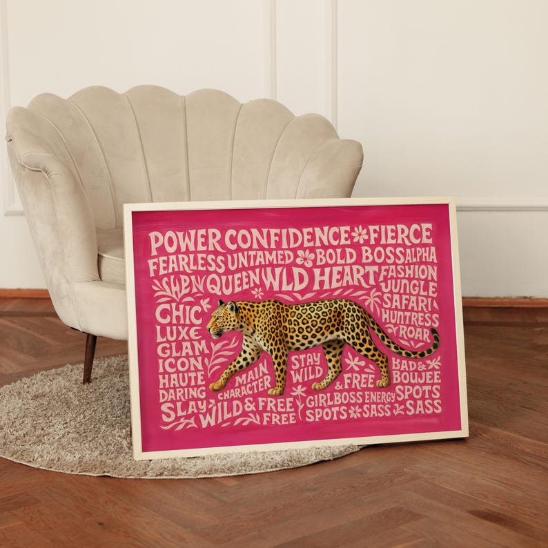 May include: A framed artwork featuring a leopard illustration on a pink background. The artwork includes text with words like "Power," "Confidence," and "Wild." The frame is white, and the artwork is displayed near a beige armchair.