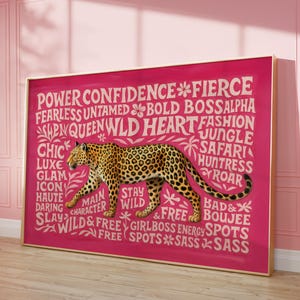 May include: A framed art print featuring a leopard illustration on a vibrant pink background. The artwork includes text with words like "Power," "Wild," and "Fierce." The frame is gold-colored, adding a touch of elegance to the piece.