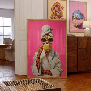 May include: A framed art print featuring a cheetah wearing sunglasses, a towel, and a robe, holding a yellow cup against a pink background. Two other framed prints are visible, one with the text "Only Good Vibes" and another with a disco ball.