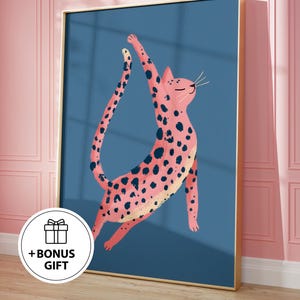 Puede incluir: Una impresión artística enmarcada que presenta un gato rosa con manchas negras sobre un fondo azul. El gato está representado con los brazos levantados. El marco es dorado. Un círculo blanco con el texto "+ BONUS GIFT" está en la esquina inferior izquierda.