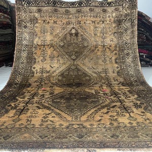May include: A large, rectangular, antique rug with a detailed, geometric pattern in shades of brown and tan. The rug features a central medallion design and intricate border. The rug is displayed on a white surface.