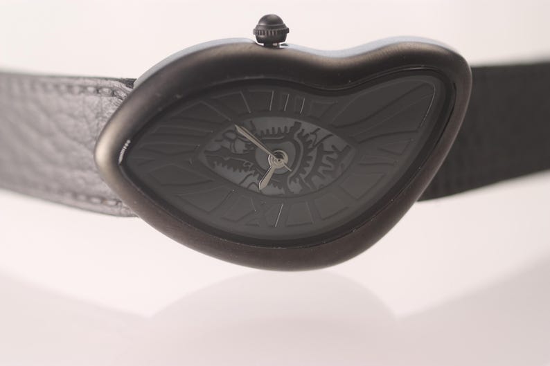 May include: A black wristwatch with a unique eye-shaped dial and a black leather band.
