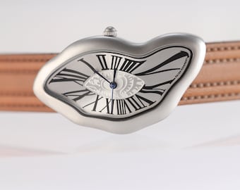 May include: A wristwatch with an irregular, melted-shape silver-tone metal case and a tan leather strap. The white dial features black Roman numerals, a central eye-shaped design, blue hands, and the text SWISS MOVEMENT.