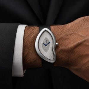 May include: A wristwatch with an asymmetrical, teardrop-shaped silver case and a textured, light gray dial. The watch features thin, dark blue hands and a small, silver crown on the right side, secured to the wrist with a smooth black strap.