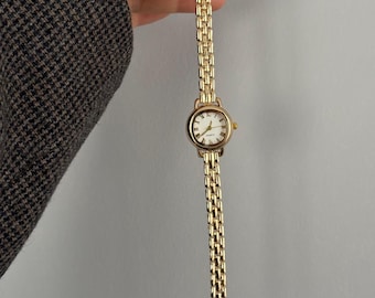 Reloj de mujer color oro, esfera con números romanos, brazalete de cuarzo.