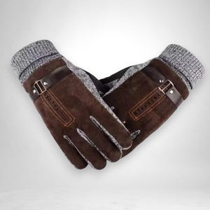 May include: Brown gloves with a suede-like texture, featuring a grey knit cuff and a brown leather strap with a metal buckle. The gloves have a warm, winter design.