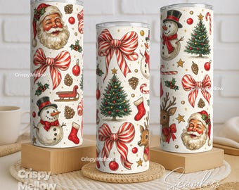 May include: Three Christmas-themed tumblers with festive designs. Each tumbler features a cream background with illustrations of Santa Claus, snowmen, Christmas trees, bows, and candy canes. The tumblers are cylindrical and stand on wooden blocks and a woven mat.
