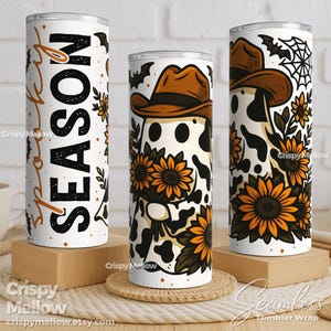 May include: Three white stainless steel tumblers with a Halloween theme. One tumbler has the word "SEASON" in black and orange. The other two tumblers feature a ghost wearing a cowboy hat, sunflowers, and bat and spiderweb graphics.