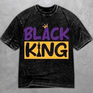 Könnte beinhalten: Schwarzes T-Shirt mit einem Used-Look. Das Design zeigt die Worte "BLACK KING" in Lila und Gelb, mit einer Krone über "BLACK" und einer Schachfigur.