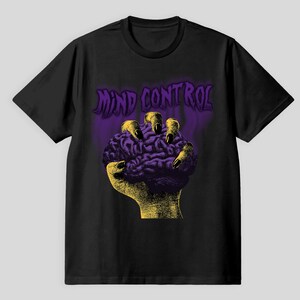 Könnte beinhalten: Schwarzes T-Shirt mit einem grafischen Design einer gelben Hand, die ein lila Gehirn umklammert. Der Text "MIND CONTROL" befindet sich in Lila über dem Gehirn. Das Design hat eine Vintage-Ästhetik mit Horror-Thema.
