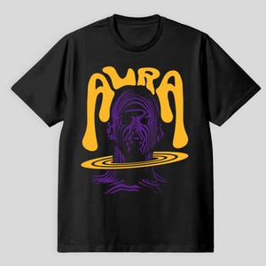 Könnte beinhalten: Schwarzes T-Shirt mit einem lila und gelben Grafikdesign. Das Design zeigt ein stilisiertes Gesicht mit dem Wort "AURA" in Gelb darüber. Das Gesicht ist von einem gelben Ring umgeben.