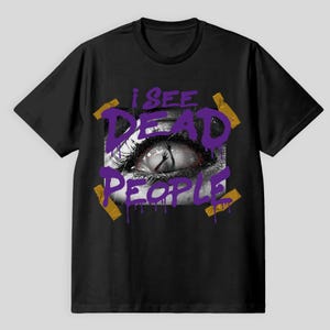 Könnte beinhalten: Schwarzes T-Shirt mit einem grafischen Design, das eine Nahaufnahme eines Auges mit dem Text "I SEE DEAD PEOPLE" in Lila zeigt. Das Design beinhaltet eine Hand, die aus dem Auge ragt und mit goldenem Klebeband akzentuiert ist.