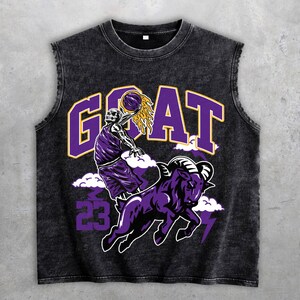 Könnte beinhalten: Schwarzes ärmelloses Shirt mit einer Grafik eines Basketball spielenden Skeletts, dem Wort "GOAT" in Lila und Gelb und einem lila Widder. Die Nummer "23" ist ebenfalls abgebildet. Das Shirt hat einen Used-Look.