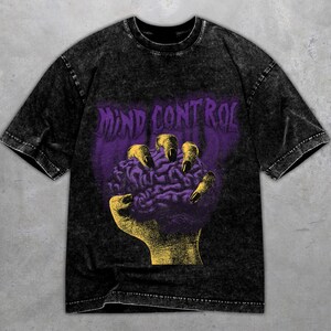 Könnte beinhalten: Schwarzes Grafik-T-Shirt mit dem lila Schriftzug "MIND CONTROL" über einer gelben Hand, die ein lila Gehirn greift. Das T-Shirt hat einen Vintage-Look.