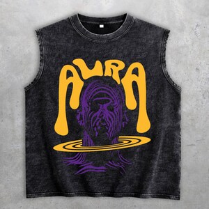 Könnte beinhalten: Schwarzes ärmelloses Shirt mit einem grafischen Design. Das Design zeigt das Wort "AURA" in Gelb, über einer lila Illustration eines Gesichts mit einem gelben Ring um den Hals. Das Shirt hat einen Vintage-Look.