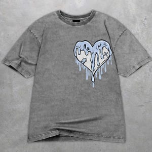 May include: Grey t-shirt with a light blue and white heart design, featuring dripping details. The graphic tee has a vintage, washed appearance and a classic crew neck.