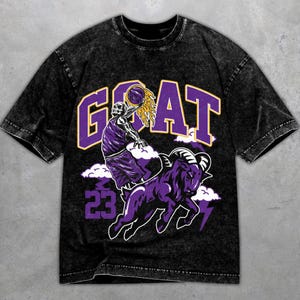 Könnte beinhalten: Schwarzes T-Shirt mit einem Grafikdesign, das ein Basketball spielendes Skelett, das Wort "GOAT" in Lila und einen lila Widder zeigt. Die Nummer "23" ist ebenfalls in Lila dargestellt. Das Shirt hat einen Vintage-Look.