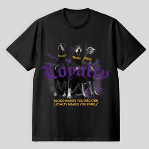 Könnte beinhalten: Schwarzes T-Shirt mit drei Dobermann-Pinschern mit goldenen Halsbändern, lila Blitzen und dem Wort "Loyalität". Der Text darunter lautet: "Blut verbindet, Loyalität macht zur Familie."
