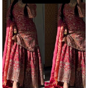 Op de afbeelding: Een tweedelige, rood en goud geborduurde outfit met een bijpassende dupatta. De outfit heeft ingewikkelde gouden borduursels en versieringen. De tekst "RiddhiSiddhiTextile" wordt bovenaan de afbeelding weergegeven. Het is een traditioneel kledingstuk.