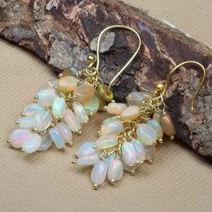Könnte beinhalten: Ein Paar goldfarbene Ohrringe mit Trauben aus ovalen Opalen. Die Opale zeigen eine Farbpalette von Weiß, schillernd bis hin zu Orange und Gelb. Die Ohrringe haben einen Hakenverschluss.