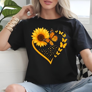 May include: Black t-shirt featuring a heart-shaped design with a yellow sunflower and orange butterfly. The design includes a cluster of yellow butterflies and yellow dots. The shirt is a casual wear item.