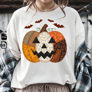 Peut inclure: T-shirt blanc à manches longues avec un motif de citrouille en patchwork. La citrouille a un visage de Jack-o'-lantern et est composée de tissus orange, marron et crème. Des chauves-souris brunes volent au-dessus, créant un thème d'Halloween.