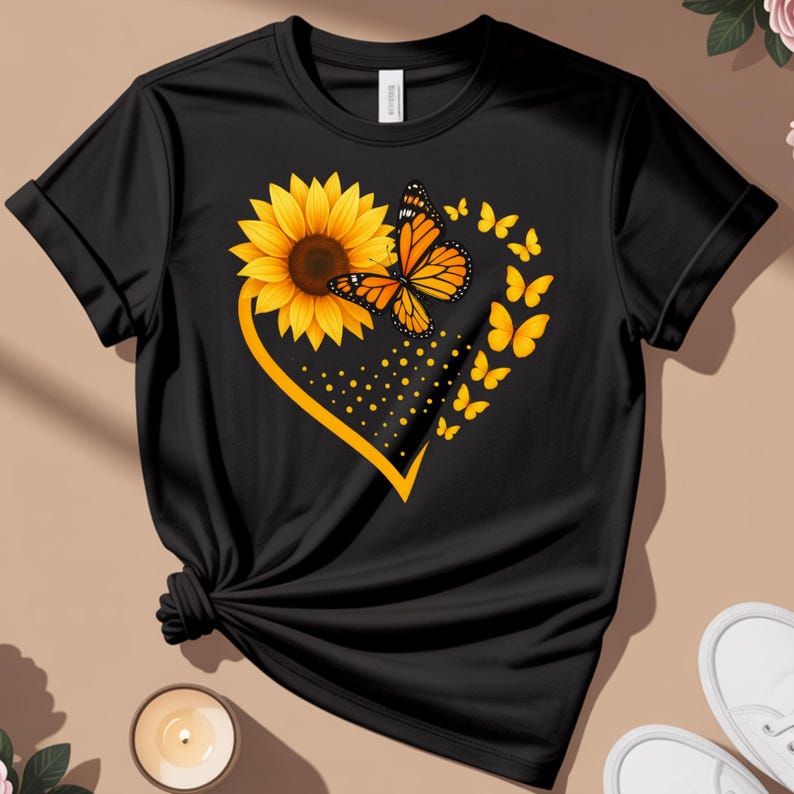 May include: Black t-shirt featuring a sunflower and monarch butterfly design. The sunflower is yellow with a brown center, and the butterfly is orange and black. A yellow heart shape surrounds the sunflower and butterfly, with yellow butterflies and dots.