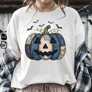 Peut inclure: T-shirt crème avec un motif citrouille patchwork bleu et beige. La citrouille a un visage sculpté et est entourée de silhouettes de chauves-souris, parfait pour Halloween. Le t-shirt est de style décontracté et confortable.