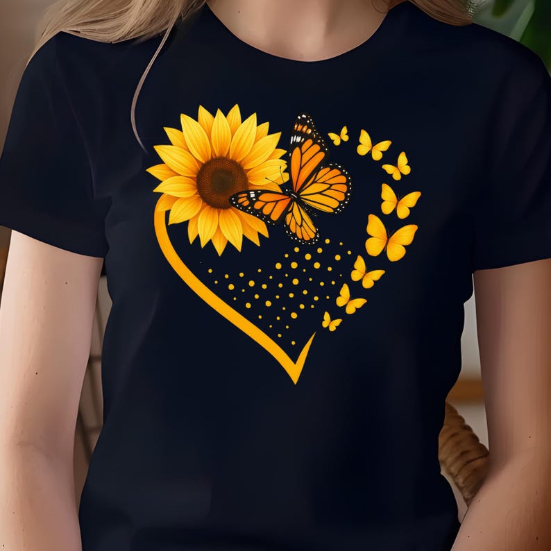 May include: Black t-shirt featuring a yellow sunflower and orange butterfly design within a yellow heart shape. The design includes smaller yellow butterflies and dots. The shirt is a classic crew neck style.
