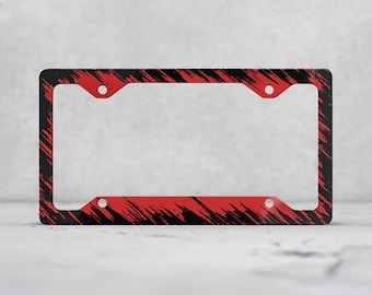 May include: A rectangular license plate frame featuring a black and red abstract brushstroke pattern. The frame has four circular mounting holes, one in each corner, and a wide border design that covers the entire perimeter of the object.