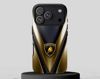 May include: Black and gold phone case with the Lamborghini logo. The case has a black top section with three camera lenses and a gold and black chevron design. The Lamborghini emblem is centered on the case.