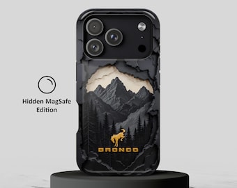 Puede incluir: Una funda de smartphone negra con un efecto de papel rasgado en capas que revela un paisaje de montaña y bosque. Una silueta de caballo dorada y el texto BRONCO están centrados. La funda incluye la etiqueta Hidden MagSafe Edition.