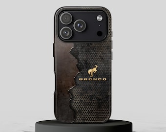 Puede incluir: Una funda para smartphone con un patrón de panal oscuro y texturizado en el lado derecho y un acabado metálico liso y desgastado en la izquierda. Un emblema de caballo Bronco dorado y el texto BRONCO están centrados en la parte posterior.