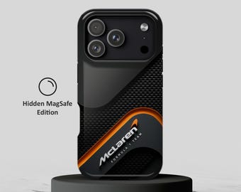 May include: A black smartphone case featuring a carbon fiber texture, a bright orange curved accent, and the McLaren Formula 1 Team logo in white. The case includes a camera cutout and is labeled as a Hidden MagSafe Edition with a circular icon.