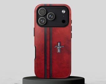May include: A red smartphone case featuring two vertical black stripes and a centered silver Mustang horse emblem with a red, white, and blue vertical bar. The case has a black camera module housing three lenses and a flash.