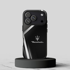 May include: Black phone case with a Maserati logo. The case has a black perforated design with silver accents and a silver Maserati emblem. The phone case is displayed on a black stand.