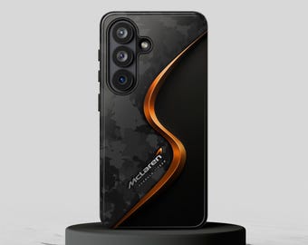 May include: A black and dark gray smartphone case featuring a carbon fiber-like pattern on the left side and a smooth matte black finish on the right, separated by a curved metallic orange line. The McLaren Formula 1 Team logo is printed in white.