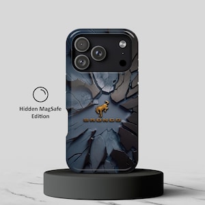 Puede incluir: Una funda para smartphone con un patrón de piedra agrietada en azul oscuro y gris, un logotipo de caballo Bronco dorado y el texto BRONCO en dorado. La funda incluye un icono circular con el texto Hidden MagSafe Edition en el lado izquierdo.