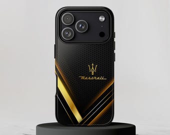 May include: A black smartphone case featuring a gold Maserati trident logo and text. The design includes a dotted pattern on the upper section and bold, diagonal gold and white lines across the lower portion, surrounding the camera module.