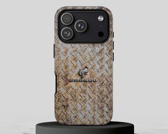 May include: A smartphone case featuring a weathered, rusted diamond plate metal texture. The center displays a silver-toned bucking horse emblem positioned above the embossed text BRONCO. The case has a black camera module cutout.