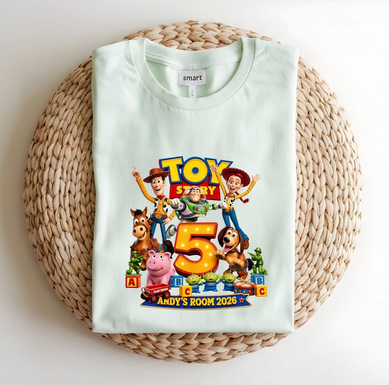 May include: A light green t-shirt featuring a Toy Story graphic with characters Woody, Buzz Lightyear, Jessie, Bullseye, Slinky Dog, Rex, and green army men surrounding a large number 5. The text reads Andy's Room 2026.