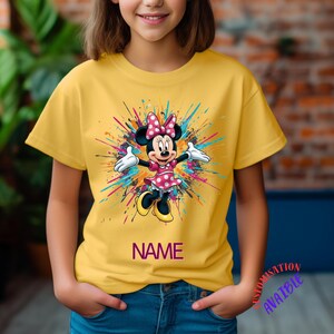 May include: Mustard yellow t-shirt with a Minnie Mouse graphic in a pink polka-dot dress and bow, set against a colourful splash. The word "NAME" is printed below. A bright and cheerful design for children.