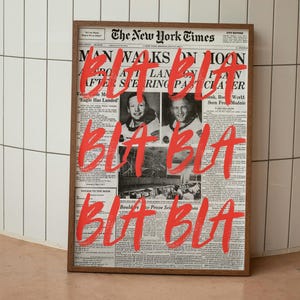 Puede incluir: Una impresión enmarcada de una portada de periódico vintage del New York Times con el titular "MAN WALKS ON MOON". Texto rojo en negrita que dice "BLA BLA" está superpuesto en la imagen. El marco es marrón.