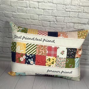 May include: Rectangular patchwork pillow with the text "First friend, best friend, forever friend." The pillow features a variety of colorful fabric squares in floral, striped, and solid patterns. The pillow has a white border with red stitching.