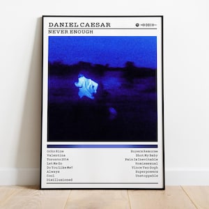 May include: A framed poster featuring the album "Never Enough" by Daniel Caesar. The artwork has a dark blue and black color scheme with a blurry image. The poster includes the album title, artist name, and a tracklist.