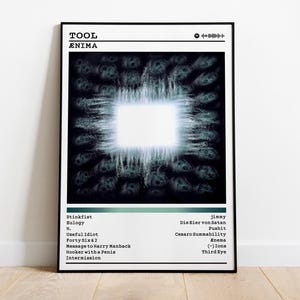May include: Black framed poster featuring the band Tool's album "Ænima". The artwork has a central white square with a glowing effect, surrounded by a dark, textured background. The band name and album title are at the top.