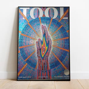 May include: Framed poster featuring the band TOOL. The artwork depicts a hand with a flame design, set against a vibrant, psychedelic background of blues, oranges, and purples. The poster includes the text "TOOL" and event details.